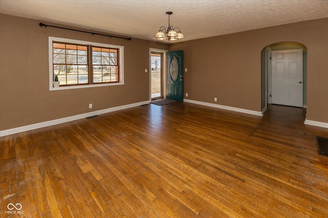 spare room with arched walkways, a notable chandelier, wood-type flooring, visible vents, and baseboards