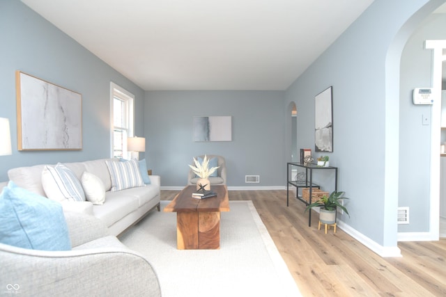 living room with arched walkways, baseboards, visible vents, and light wood-style floors