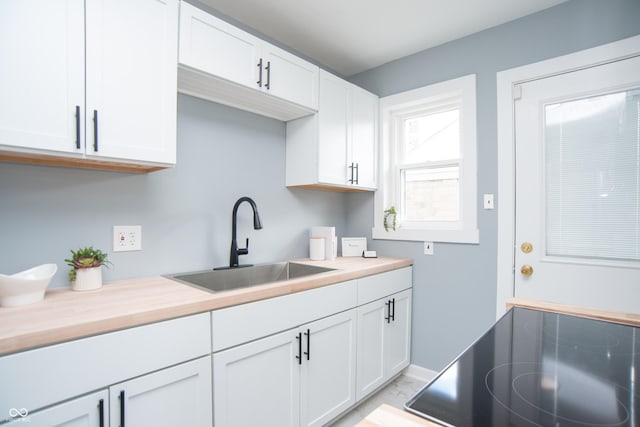 kitchen featuring black electric stovetop, a sink, white cabinetry, baseboards, and light countertops