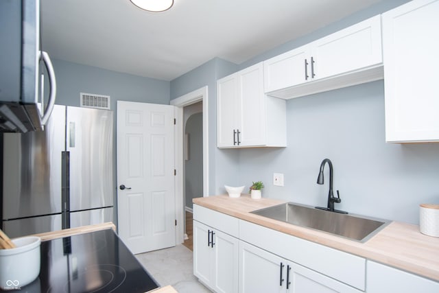 kitchen featuring freestanding refrigerator, white cabinets, a sink, and arched walkways