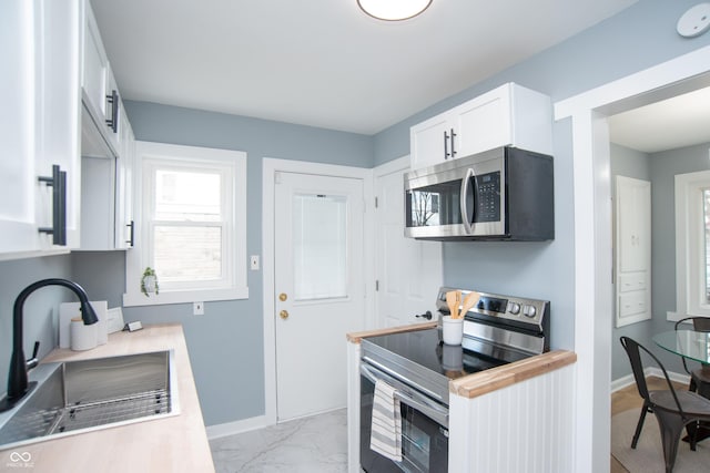 kitchen featuring baseboards, appliances with stainless steel finishes, marble finish floor, white cabinetry, and a sink