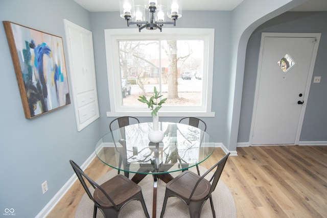 dining area with light wood-type flooring, a notable chandelier, arched walkways, and baseboards