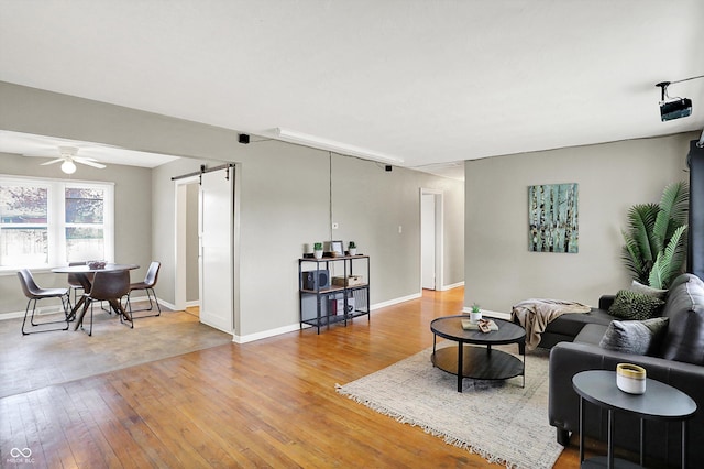 living area featuring light wood-style floors, ceiling fan, baseboards, and a barn door