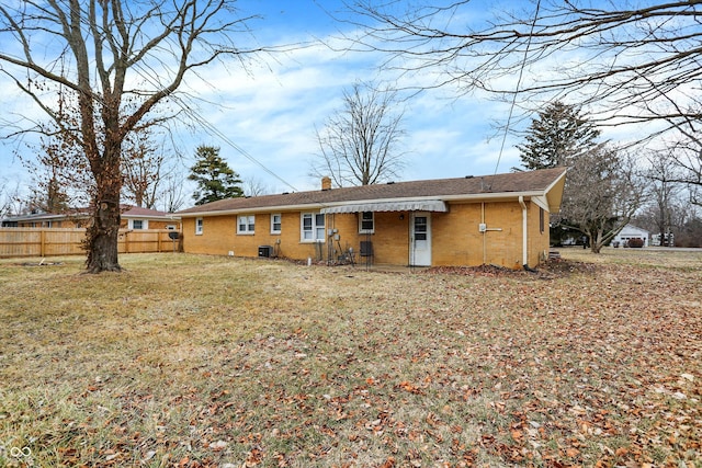 back of property with cooling unit, brick siding, fence, a lawn, and a chimney