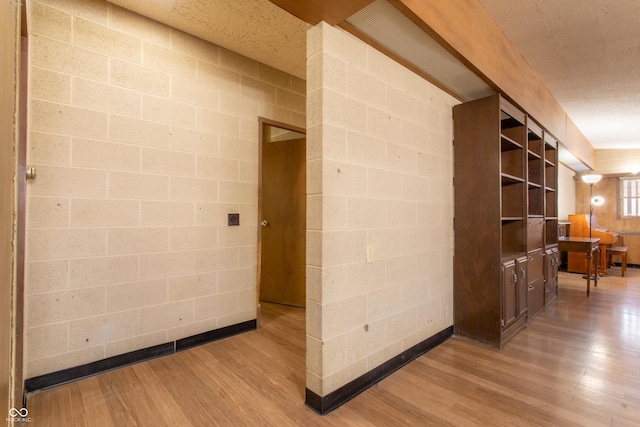 hall with wood finished floors and concrete block wall