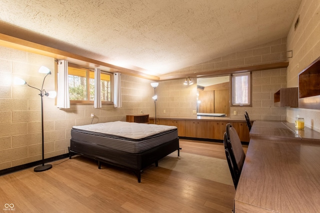 bedroom with concrete block wall, lofted ceiling, visible vents, a textured ceiling, and light wood-type flooring