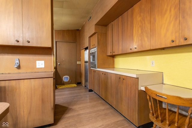 kitchen featuring oven, visible vents, light wood-style floors, light countertops, and brown cabinetry