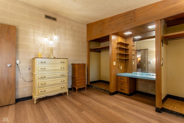 interior space with concrete block wall, a textured ceiling, baseboards, and wood finished floors