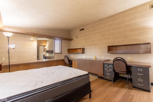 bedroom with light wood-type flooring, visible vents, built in study area, and a textured ceiling