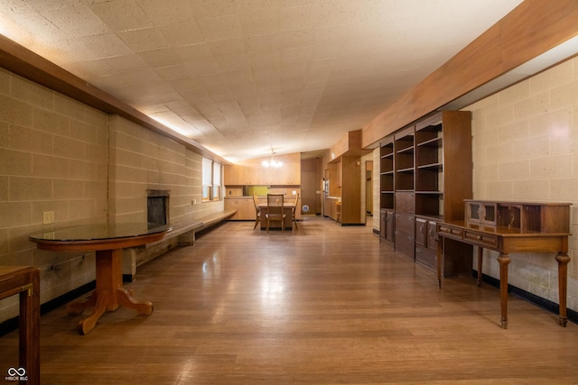 interior space featuring a chandelier, vaulted ceiling, wood finished floors, and concrete block wall