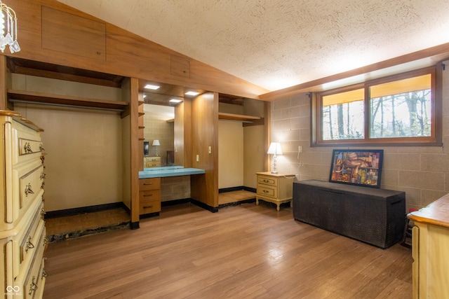 bedroom featuring concrete block wall, vaulted ceiling, light wood-style flooring, and a textured ceiling