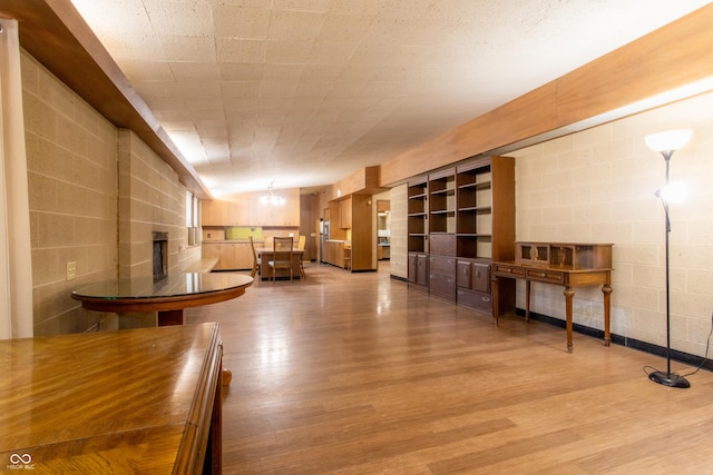 unfurnished dining area featuring concrete block wall, a notable chandelier, a fireplace, and light wood-style flooring