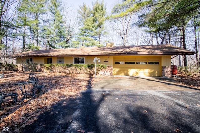 ranch-style home featuring brick siding, driveway, a chimney, and an attached garage