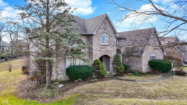 view of front of property with a shingled roof, brick siding, and a front lawn