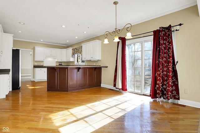 kitchen featuring a peninsula, light wood-style floors, freestanding refrigerator, dark countertops, and crown molding