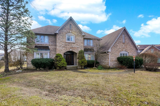 view of front of house with roof with shingles, brick siding, and a front lawn