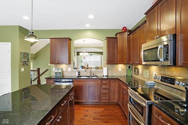 kitchen featuring tasteful backsplash, appliances with stainless steel finishes, dark stone countertops, dark wood-type flooring, and a sink