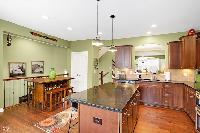 kitchen featuring arched walkways, a kitchen island, a kitchen breakfast bar, dark wood-type flooring, and a sink