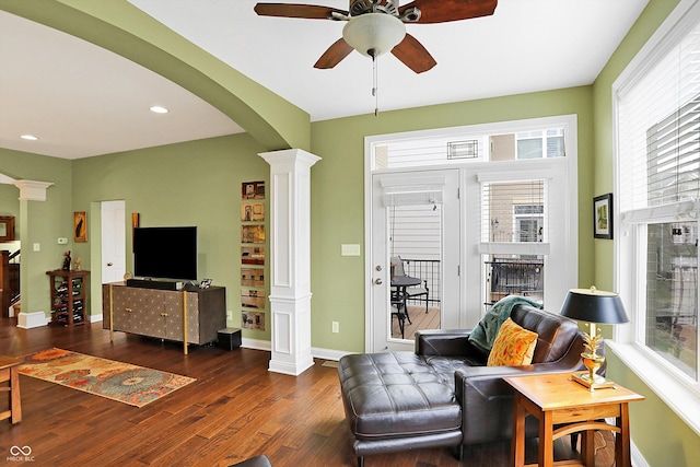 living room featuring arched walkways, wood finished floors, decorative columns, and a healthy amount of sunlight