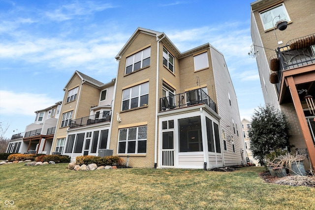 rear view of house featuring a balcony, a sunroom, cooling unit, a yard, and brick siding