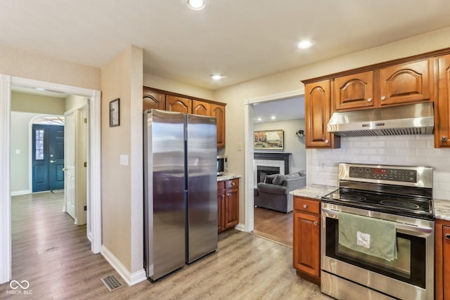 kitchen featuring under cabinet range hood, visible vents, appliances with stainless steel finishes, decorative backsplash, and light wood finished floors