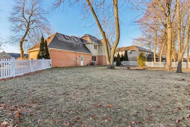 back of house featuring a fenced backyard, a lawn, and brick siding