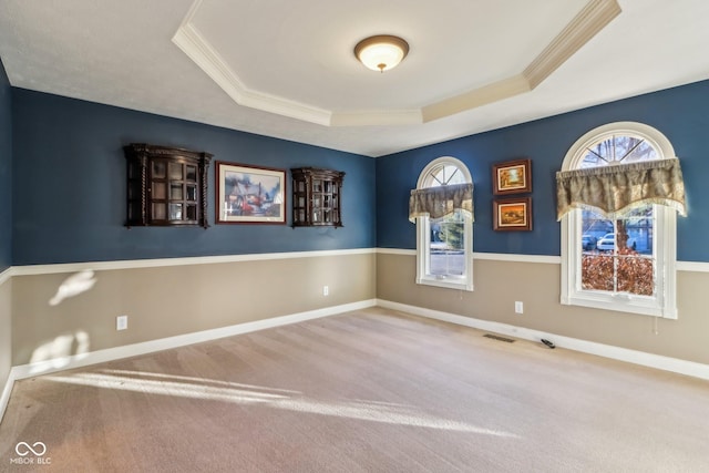 carpeted spare room with crown molding, a raised ceiling, visible vents, and baseboards