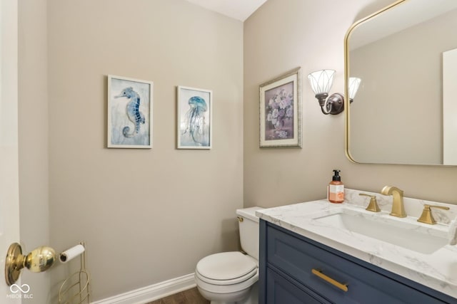 half bathroom featuring toilet, vanity, baseboards, and wood finished floors