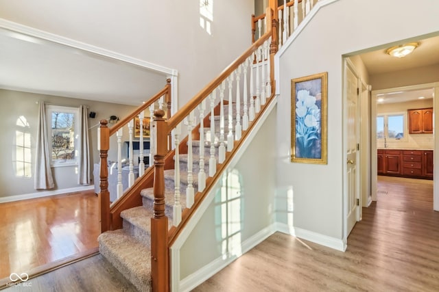 stairway featuring a towering ceiling, baseboards, and wood finished floors