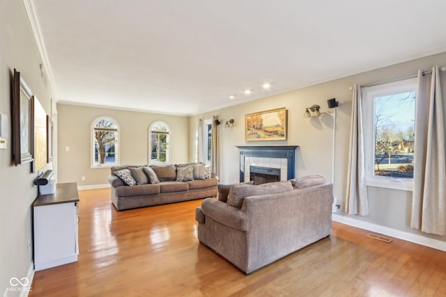 living room featuring light wood finished floors, a fireplace, visible vents, and ornamental molding