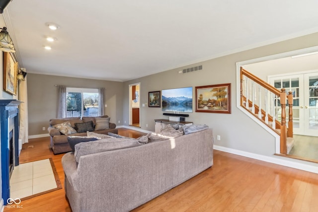 living room with visible vents, stairs, crown molding, light wood-style floors, and a fireplace