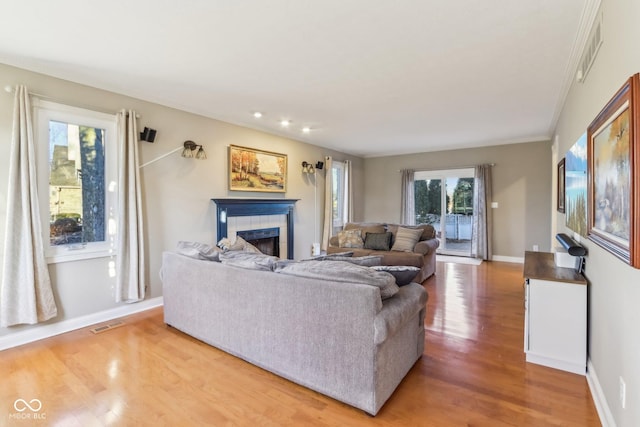 living room featuring baseboards, visible vents, light wood-style flooring, and a tiled fireplace