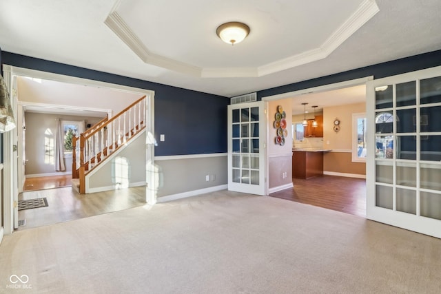 carpeted spare room with stairway, a tray ceiling, and ornamental molding