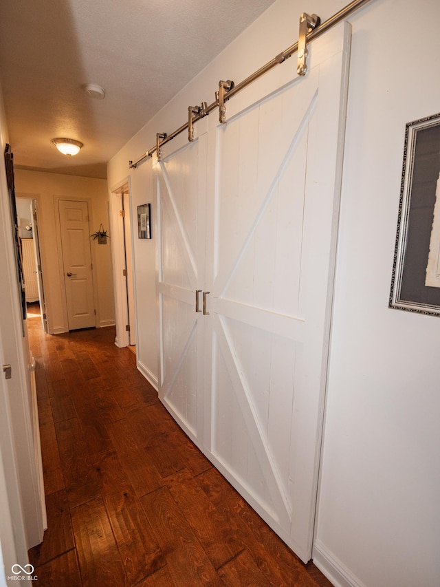 corridor featuring a barn door, baseboards, and wood-type flooring