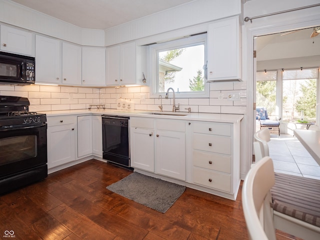 kitchen with dark wood-style flooring, a sink, white cabinetry, light countertops, and black appliances