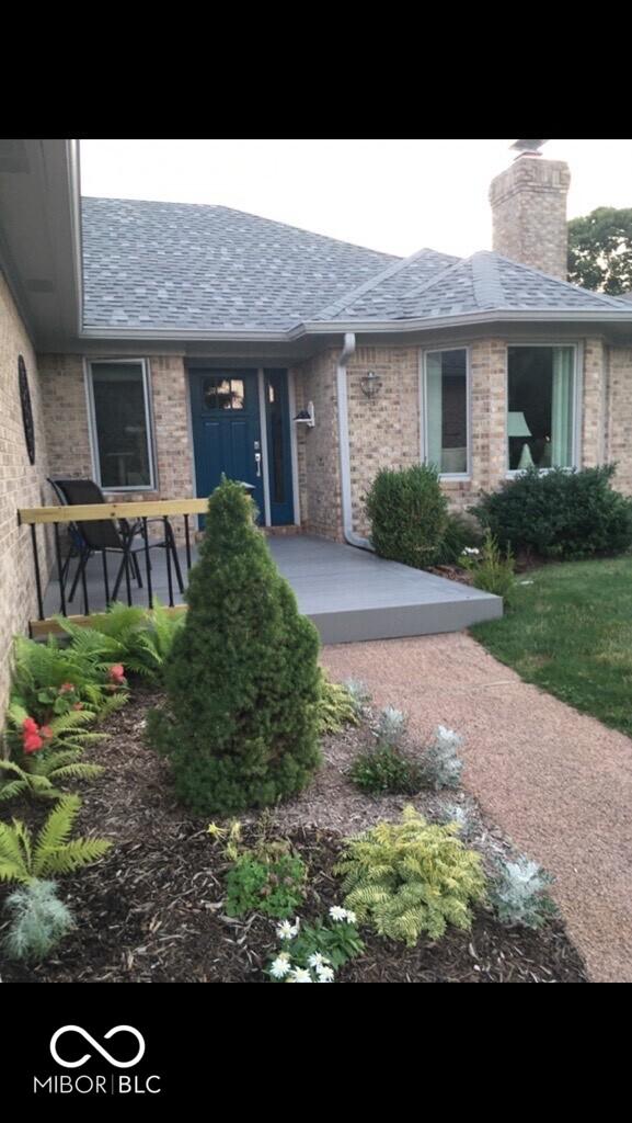 entrance to property featuring roof with shingles, brick siding, and a chimney