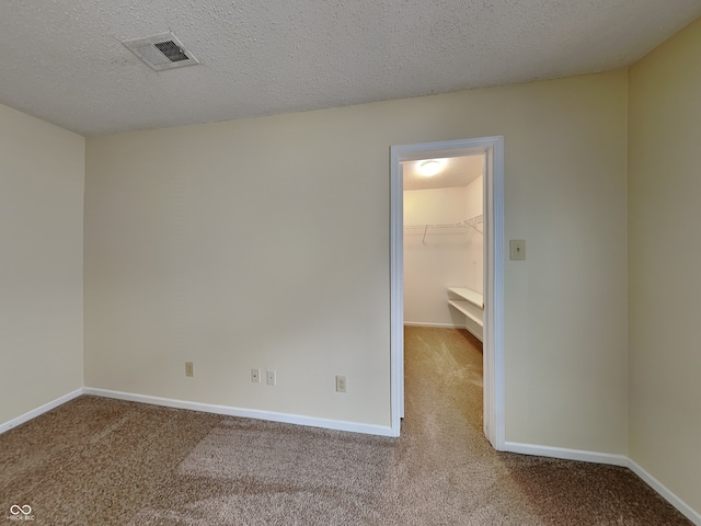 unfurnished bedroom with a textured ceiling, visible vents, a walk in closet, and carpet flooring