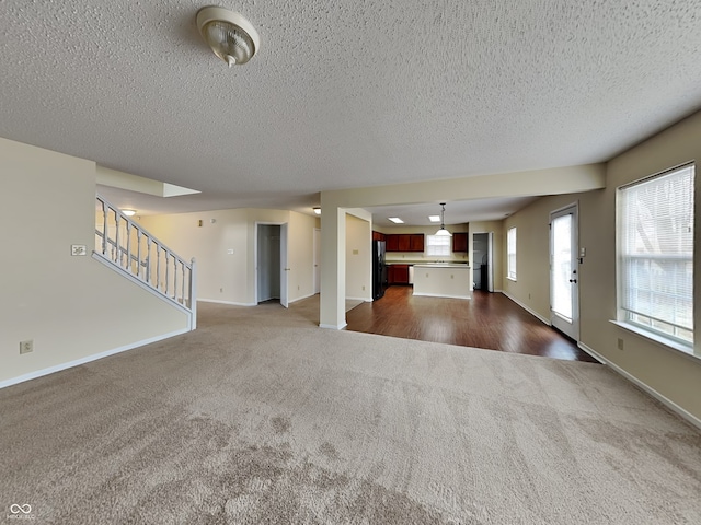 unfurnished living room with baseboards, stairway, dark carpet, and a textured ceiling