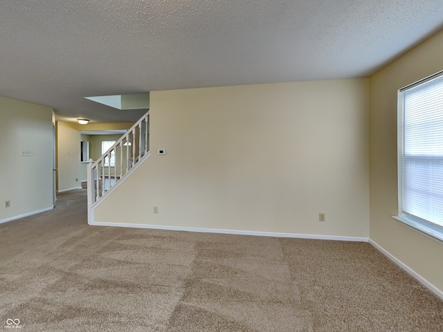 carpeted spare room with stairs, a textured ceiling, and baseboards