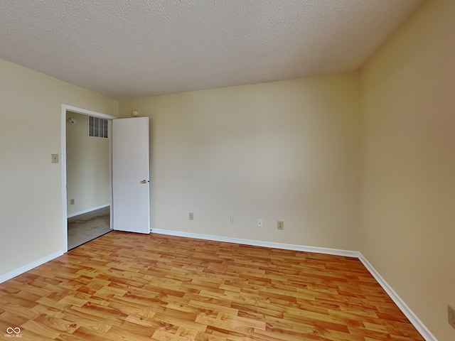 spare room with a textured ceiling, light wood finished floors, visible vents, and baseboards