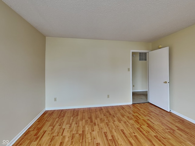 spare room featuring visible vents, light wood-style flooring, baseboards, and a textured ceiling