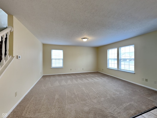 empty room featuring light colored carpet, a textured ceiling, and baseboards