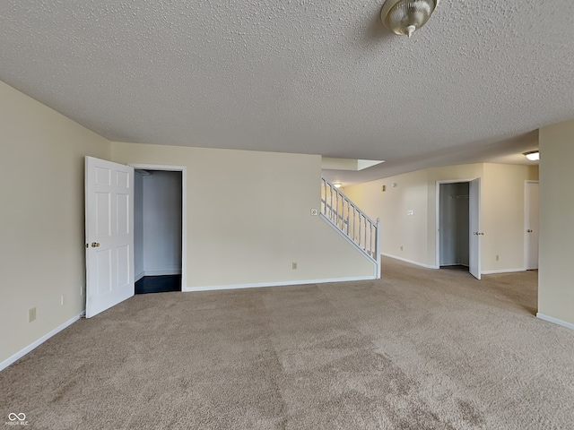 carpeted empty room featuring a textured ceiling, stairway, and baseboards