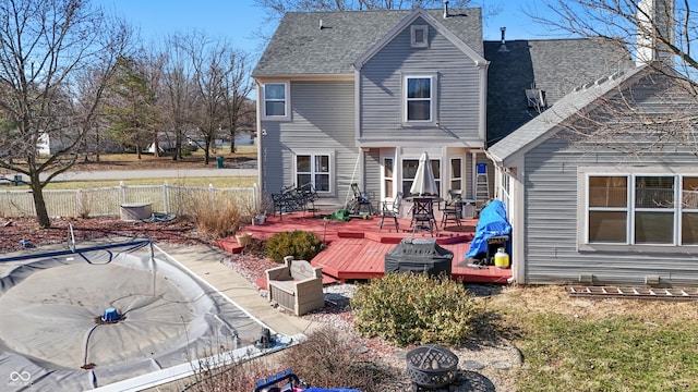 back of property with a shingled roof, a wooden deck, and fence