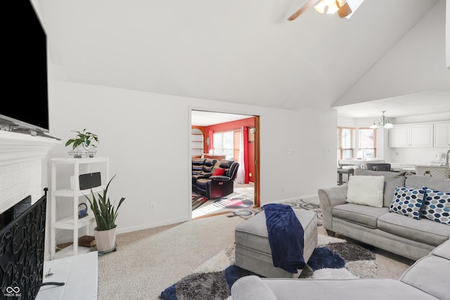 carpeted living room featuring baseboards, high vaulted ceiling, a brick fireplace, and ceiling fan with notable chandelier