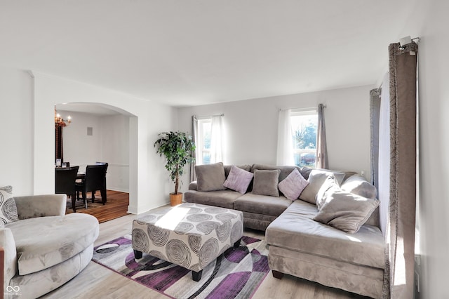 living area featuring light wood-style flooring, a notable chandelier, and arched walkways