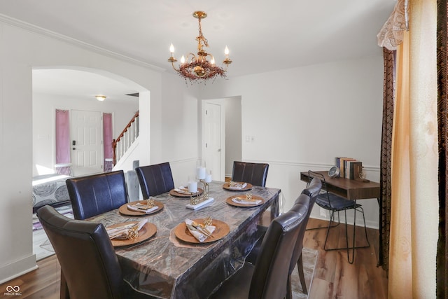 dining room featuring an inviting chandelier, stairway, wood finished floors, and arched walkways