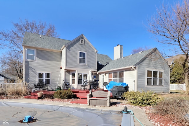 rear view of property with a deck, fence, roof with shingles, and a chimney