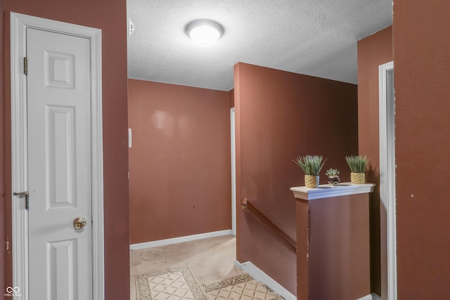 hallway with baseboards, an upstairs landing, and a textured ceiling