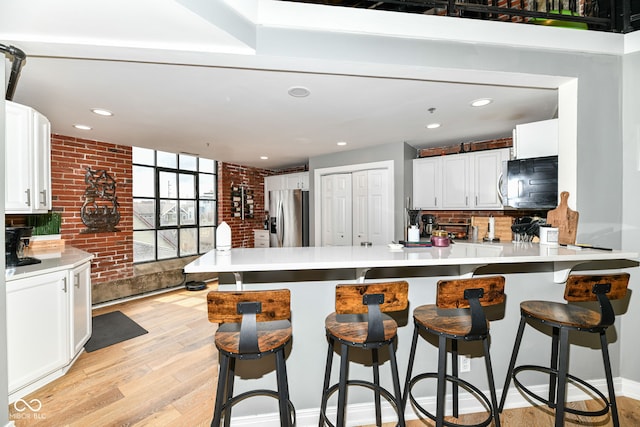 kitchen with a peninsula, light wood-style floors, brick wall, and stainless steel fridge with ice dispenser